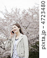 桜をバックにスマートフォンで通話をする女性