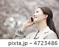 桜をバックにスマートフォンで通話をする女性