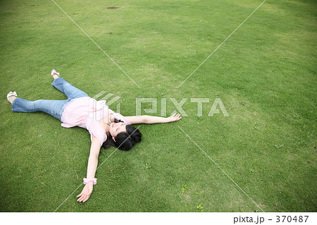 芝生の上で大の字になって寝る女性の写真素材