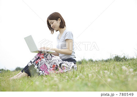 草原に座りパソコンする女性の写真素材