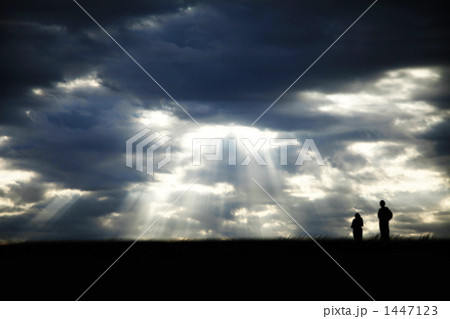 雲の隙間から差し込む神々しい光を見上げるカップルの写真素材