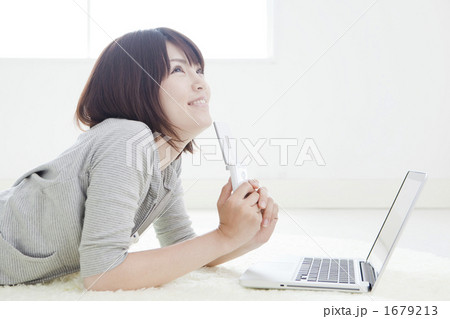 パソコンの前で携帯を持つ女性 1679213