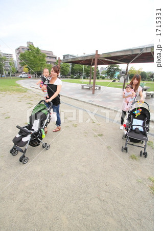 赤ちゃんを抱きベビーカーを押して公園を散歩する2組の若い親子 赤ちゃんを抱きベビーカーを押して公園を散歩する2組の若い親子 1715331