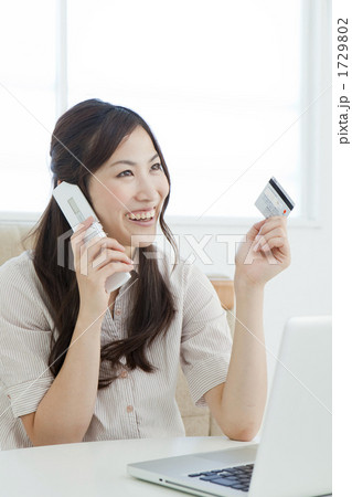 パソコンの前でクレジットカードを持って電話をする若い女性 1729802