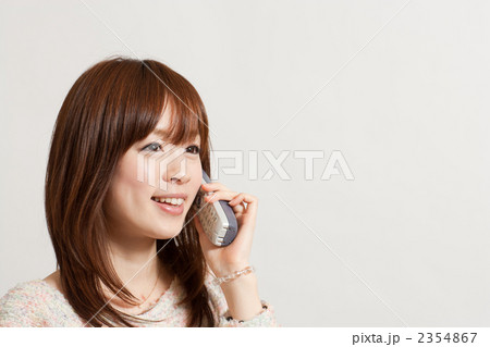 白い背景の前で楽しそうに電話で会話する笑顔の若い女性 白い背景の前で楽しそうに電話で会話する笑顔の若い女性 2354867