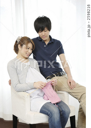 窓辺で編み物をする妊婦と見つめる夫 2598216