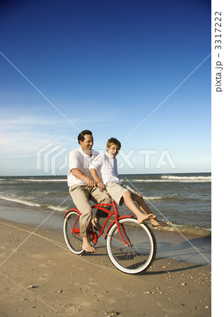 Dad riding red bicycle with son on handlebars. 3317222