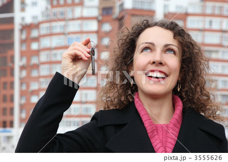 young girl with key in hand looks upwards against many-storeyed 3555626