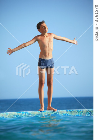 teenager boy standing near pool against sea, Plants hands in par teenager boy standing near pool against sea, Plants hands in par 3561570