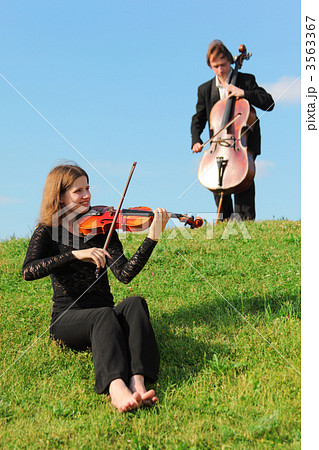 violinist and violoncellist play on grass against sky 3563367
