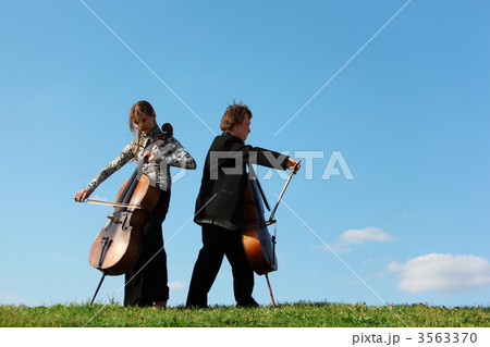 Two violoncellists play on grass against  sky 3563370