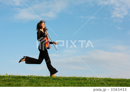 girl with violin runs on grass against  sky, side view 3563433