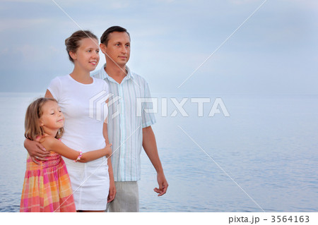 Happy family with little girl standing on beach in evening 3564163