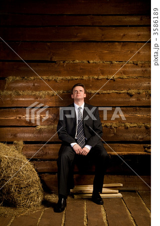 lonely businessman sitting on bench near haystack in wooden log 3586189