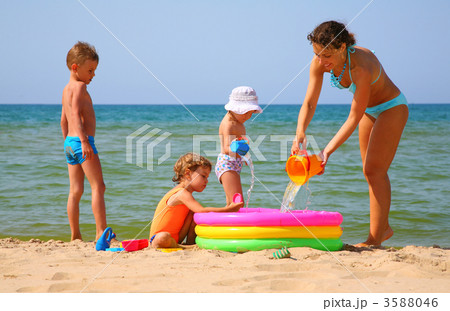 Mother with children to pour water in inflatable pool on shore of sea 3588046