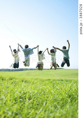 草原でジャンプをする若者たちの後姿の写真素材