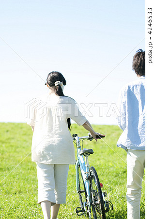 草原で自転車を押すカップルの後姿の写真素材