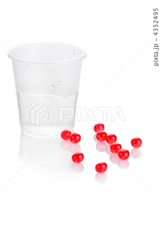 Pharmacy. Red vitamin pills and plastic cup of water on white ba 4352495