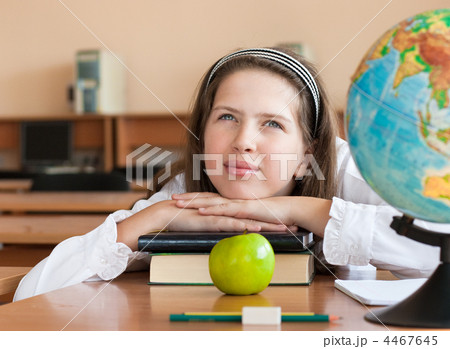 Schoolgirl's portrait at school desk with her books and globe 4467645