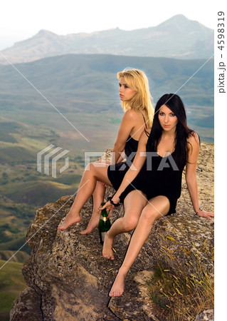 Two young women with a champagne bottle sit on a rock Two young women with a champagne bottle sit on a rock 4598319