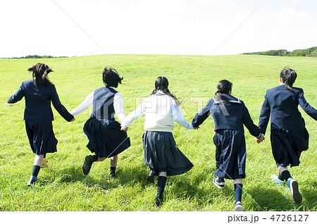 草原で手をつなぎ走る中学生の後姿の写真素材