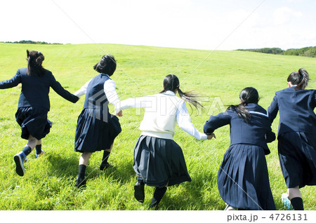 草原で手をつなぎ走る中学生の後姿の写真素材