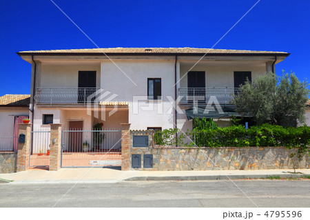 Facade of fenced white two-story cottage with garden and balcony Facade of fenced white two-story cottage with garden and balcony 4795596