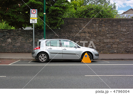 Car street clamped with yellow metal wheel clamp. Trees grow beh 4796004
