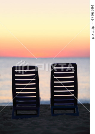 Two empty chairs stand on sand near sea during sunset Two empty chairs stand on sand near sea during sunset 4796994
