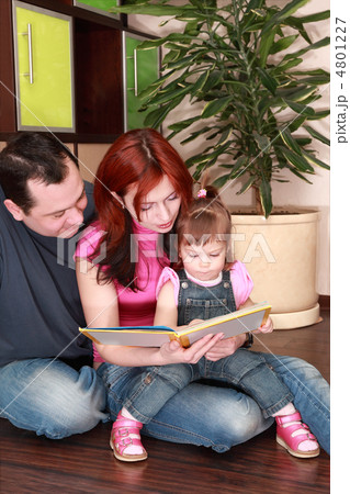 mother, father and little daughter in denim jumpsuit reads book 4801227