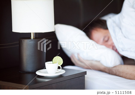 man sleeping on a bed, a cup of tea on the bedside table and lam 5111508