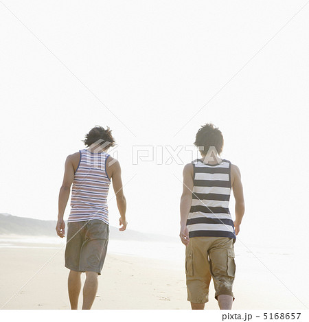 砂浜を歩く男性2人の後ろ姿の写真素材