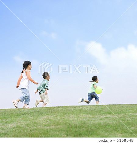 丘の上を走る子供達の後ろ姿の写真素材