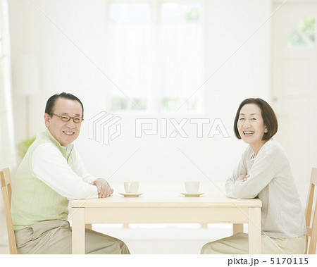 テーブルに向かい合って座るシニア夫婦の写真素材