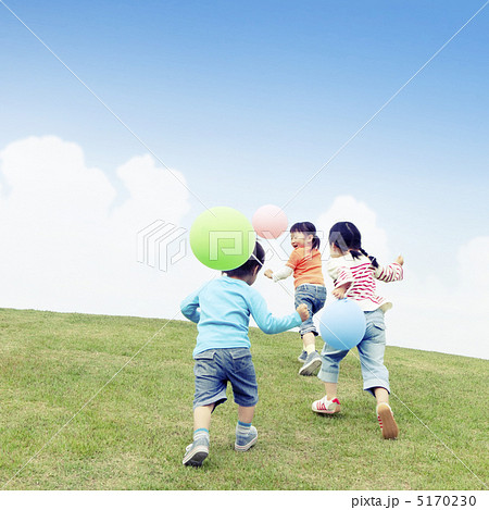 風船を持って丘を走る子供達の後ろ姿の写真素材