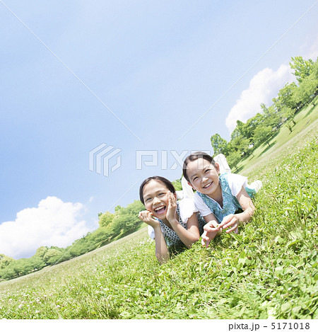 草原に寝転んで頬杖をつく二人の女の子 5171018