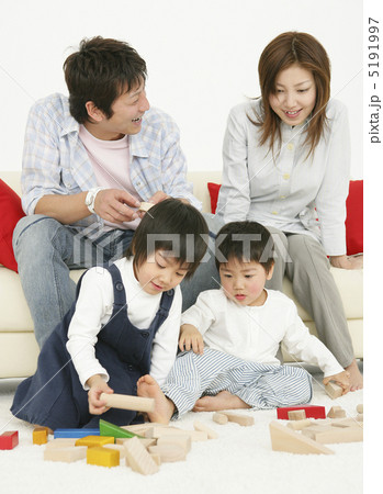ソファに腰掛け床で積み木遊びをする娘と息子を眺める若い夫婦 ソファに腰掛け床で積み木遊びをする娘と息子を眺める若い夫婦 5191997