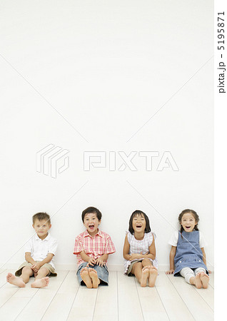 壁にもたれて座る子供達の写真素材