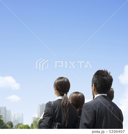 青空を見上げる4人のビジネスマンとビジネスウーマンの後ろ姿の写真素材