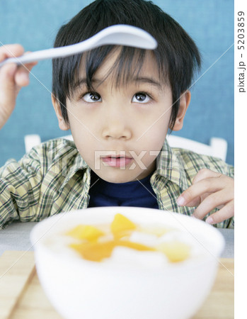 テーブルの杏仁豆腐を前にスプーンを見つめる少年 5203859