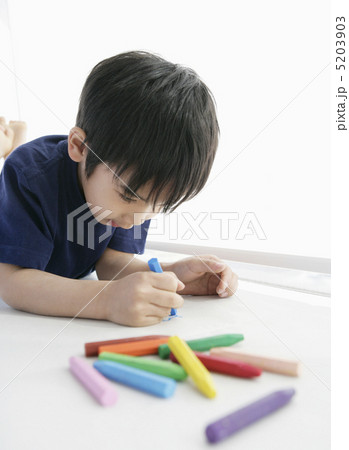 寝転んでオイルパステルで絵を描く少年 5203903