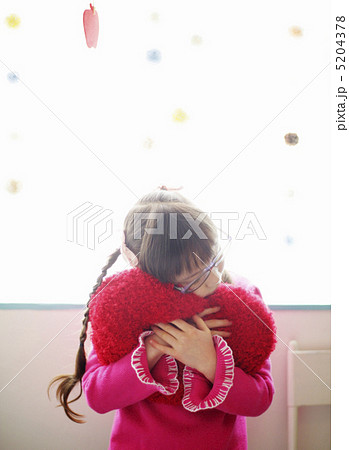ハートのクッションを抱きしめる女の子の写真素材