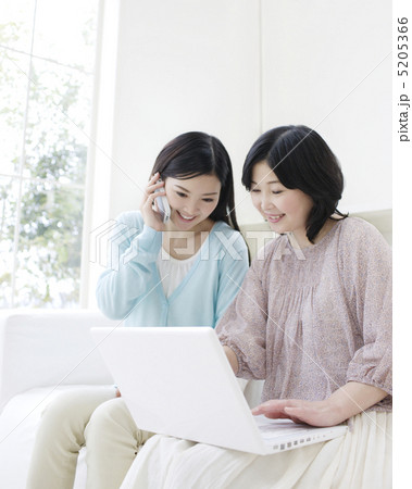 パソコンを操作する母と携帯電話で話す娘 5205366