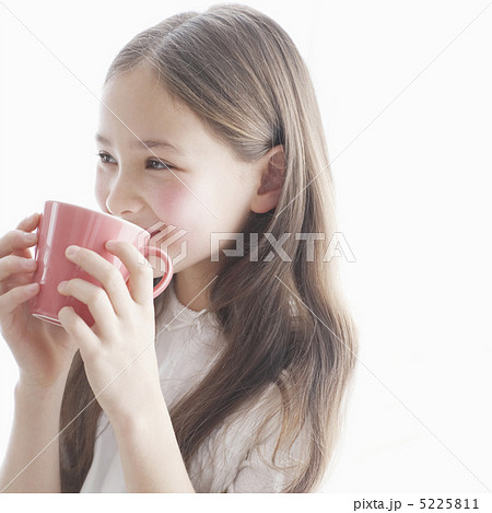 マグカップで飲み物を飲む笑顔の少女の写真素材