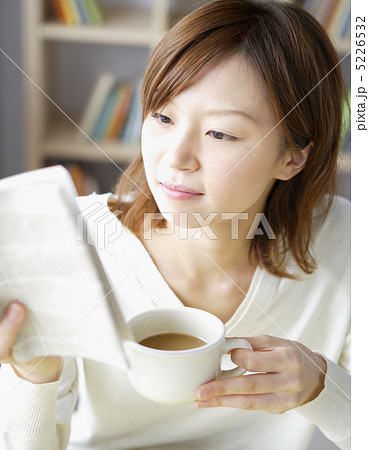 カップを片手に本を読む女性の写真素材