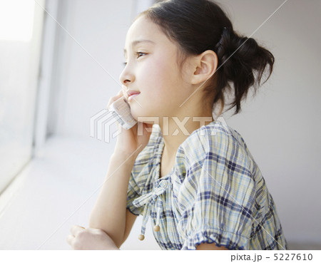 窓にもたれて携帯電話で話す少女 5227610