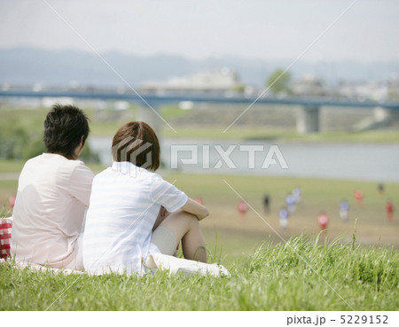 土手に並んで座るカップルの写真素材