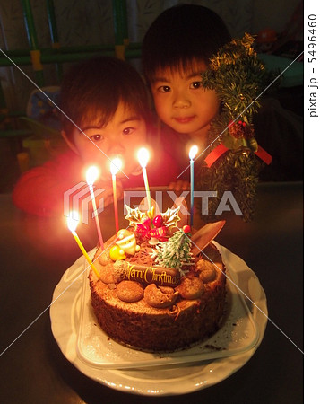 ろうそくの灯ったクリスマスケーキを兄弟で見つめる画の写真素材