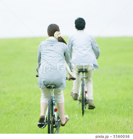 草原で自転車に乗るカップルの後姿の写真素材