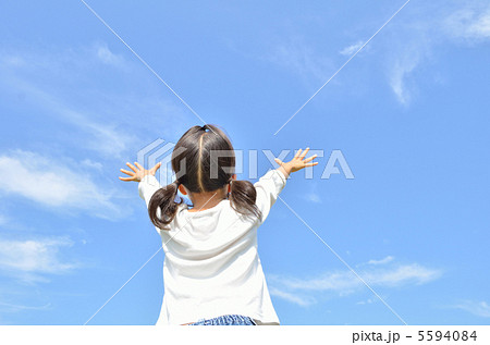青空でバンザイする女の子 後ろ姿 の写真素材